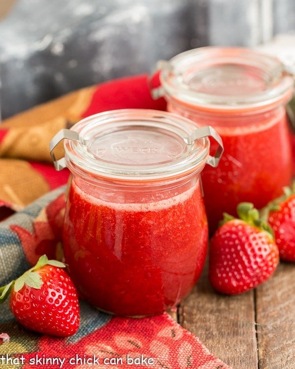 2 small Weck jars filled with homemade strawberry sauce, surrounded by fresh strawberries.