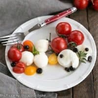 Overhead view of a white plate of burrata Caprese salad with balsamic pearls