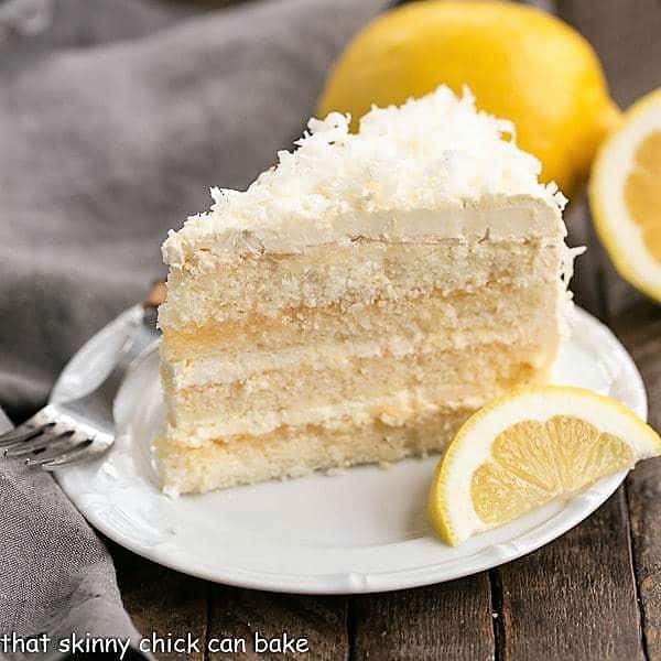 Lemon Layer Cake with Lemon Curd Filling slice on a white ceramic plate with a lemon wedge.