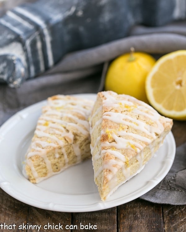 Two Glazed Lemon Tea Scones on a white plate with lemons in the background,