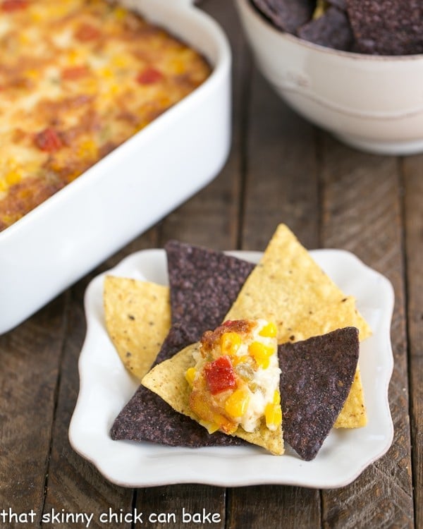 Fiesta Corn Dip - With a double dose of gooey cheese, you'll want to serve this magnificent dip at every gathering! Fiesta Corn Dip on a chip on a white white.