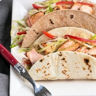 Two Salmon Tacos with Mango Salsa on a square white plate with a red handled fork