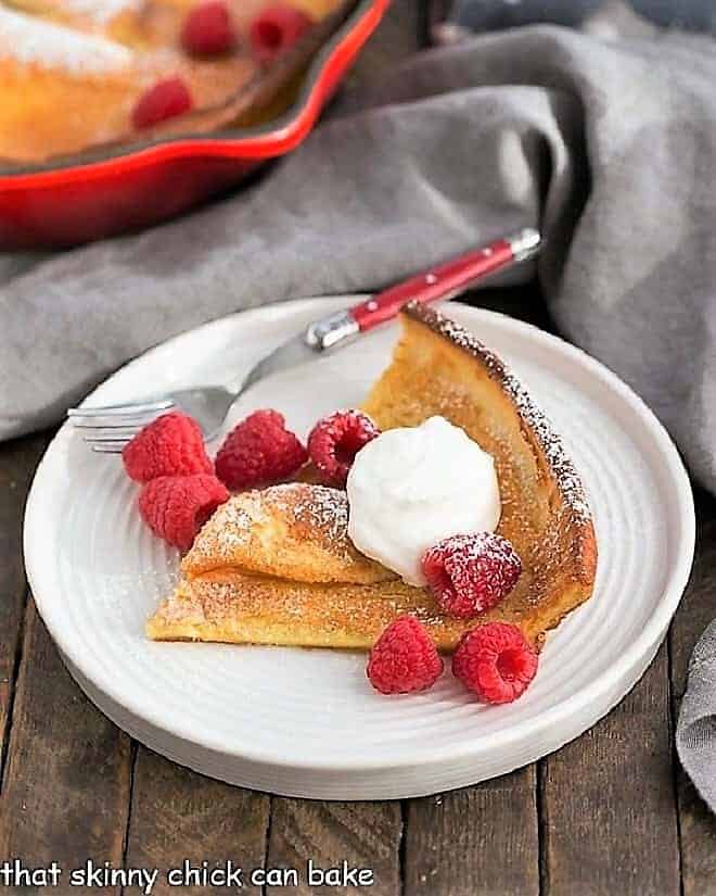 Best Dutch Baby Pancake slice on a white plate topped with cream and raspberries.