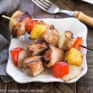 Honey Glazed Chicken Kabobs on a small square white plate, one skewer and loose chicken and pineapple pieces