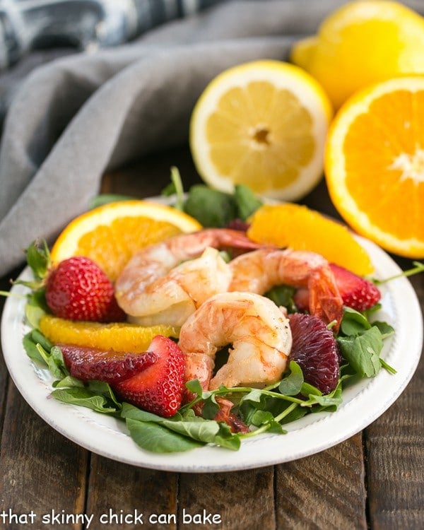 Shrimp, Orange, & Watercress Salad with Citrus Vinaigrette on a white plate with cut citrus in the background