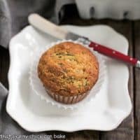Overhead view of one cinnamon zucchini muffin on a white plate with a red handle knife