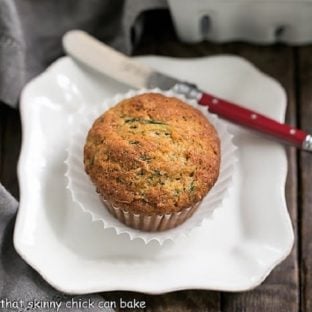 Overhead view of one cinnamon zucchini muffin on a white plate with a red handle knife