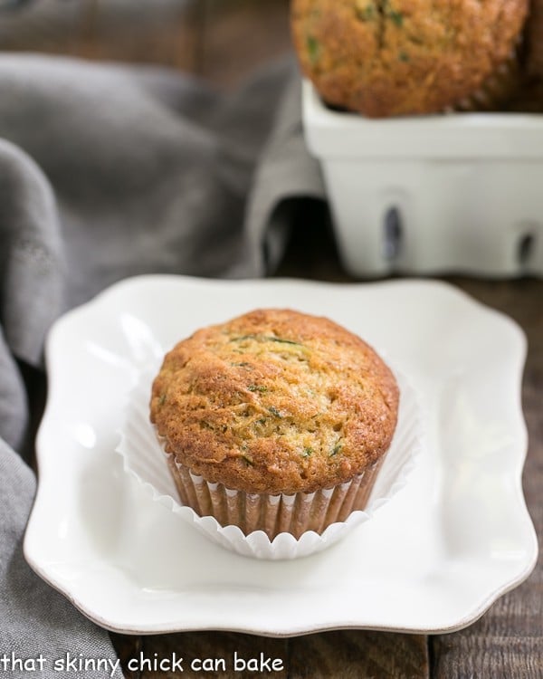 Cinnamon Zucchini Muffins on a white plate with a square basket of muffins in the background