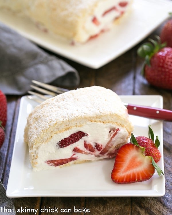 Strawberry Filled Meringue Roulade slilce on a square white plate with a red handled fork and strawberry garnish