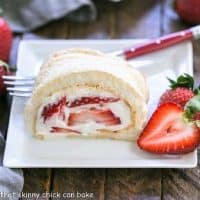 Slice of strawberry filled meringue roulade on a square white plate with a fork and berry garnish
