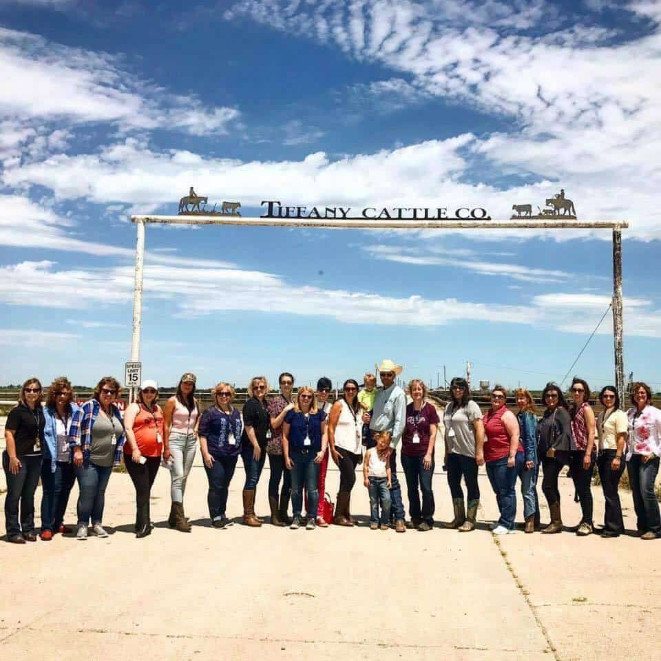 A group of people standing in front of the sign to a cattle ranch.