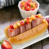 Bacon Wrapped Hot Dogs with Fruit Salsa on a narrow white ceramic plate