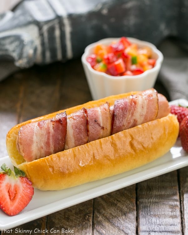 Bacon Wrapped Hot Dogs with Fruit Salsa on a rectangular plate with a ramekin of salsa