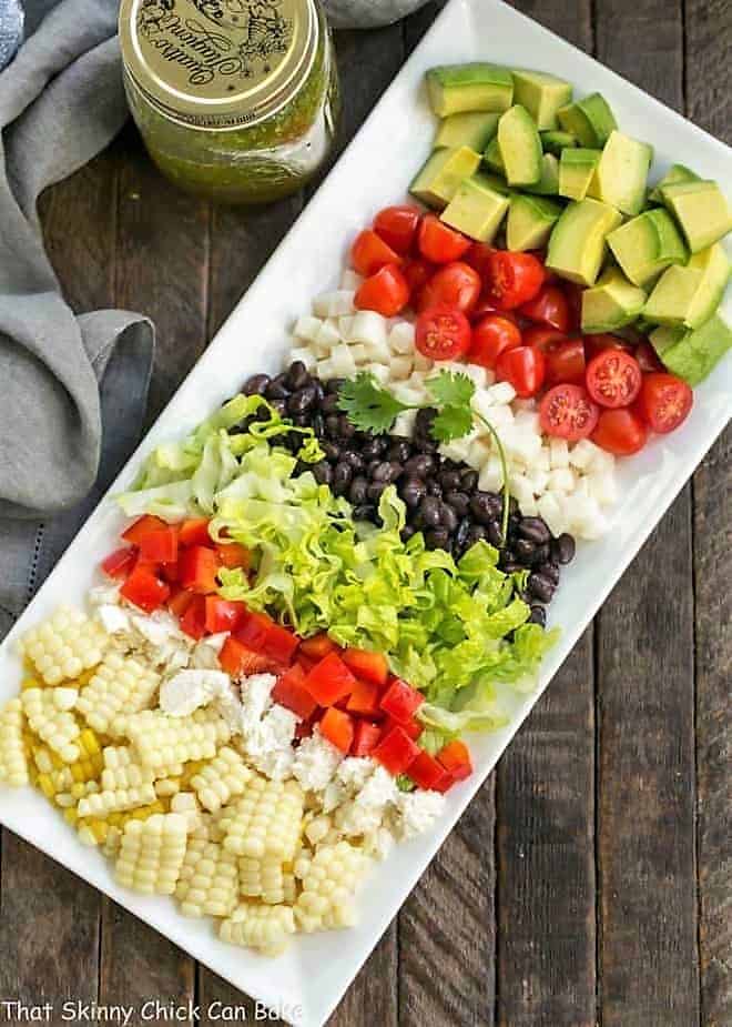Overhead view of Mexican Chopped Salad on a rectangular white tray plus dressing in a canning jar.