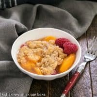 Peach raspberry crisp in a small white bowl with fresh raspberry garnish and a red handle fork