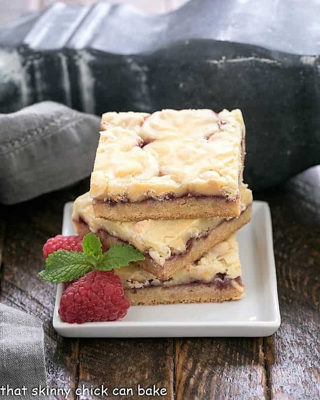 A stack of white chocolate raspberry bars on a square white plate with raspberries and mint to garnish.