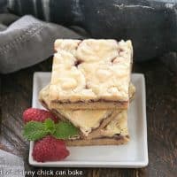 A stack of 3 white chocolate raspberry bars on a square white plate with raspberries and mint to garnish