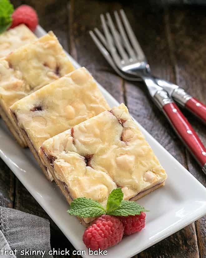 White choolate raspberry bars on a white tray with raspberries and mint.