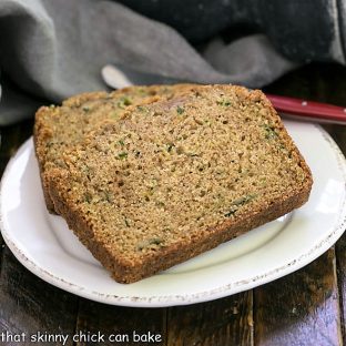 Two slices of zucchini bread on a round white plate with a red handle knife