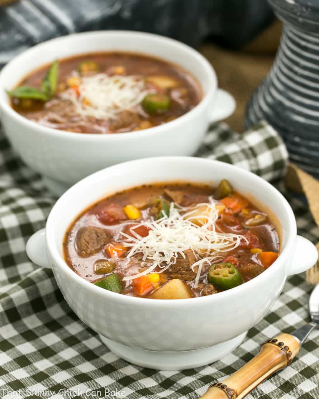 Two bowls of Vegetable Beef Soup in white soup bowls on a green and white checked napkin.