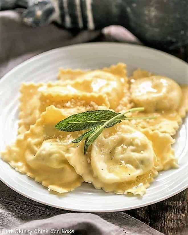 Ravioli on a white plate with sage leaves to garnish