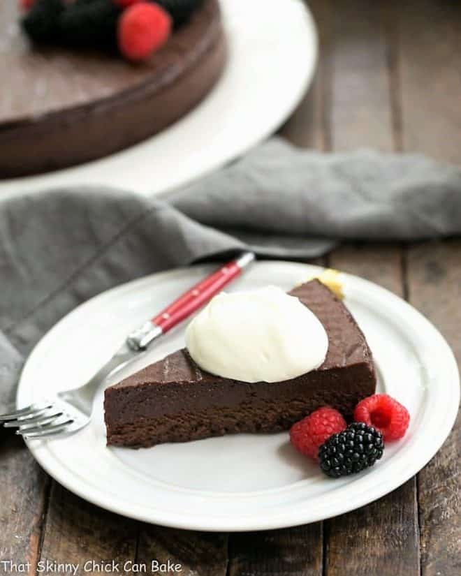 Slice of Flourless Cake Chocolate topped with whipped cream on a round white dessert plate with a red handled fork