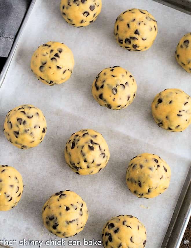 12 large chocolate chip cookie dough balls on a sheet pan.