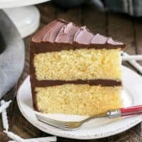 Classic Yellow Butter Cake with chocolate Icing on a white plate with a red handled fork
