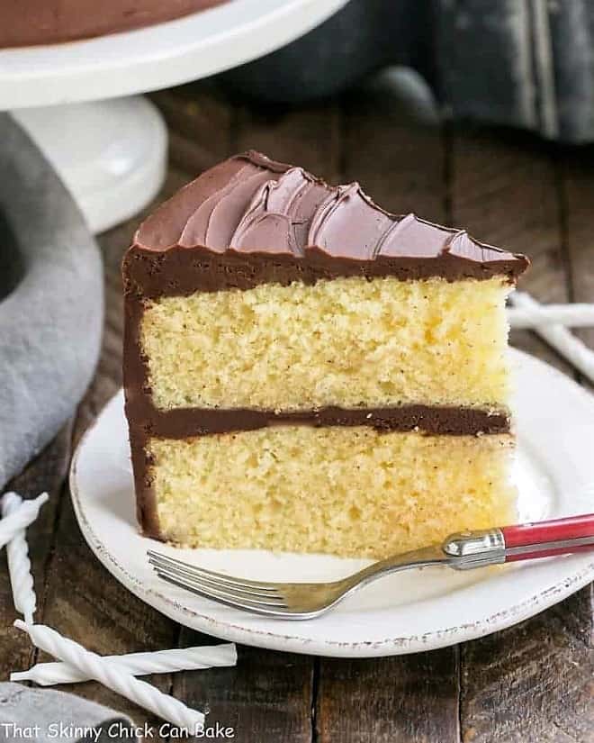 Classic Yellow Butter Cake with chocolate Icing on a white plate with a red handled fork