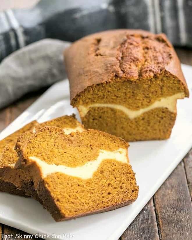 Cream Cheese Filled Pumpkin Bread -A moist, delicious pumpkin loaf with a ribbon of cream cheese in the middle! Cream Cheese Filled Pumpkin Bread on a white ceramic board with sliced pieces.
