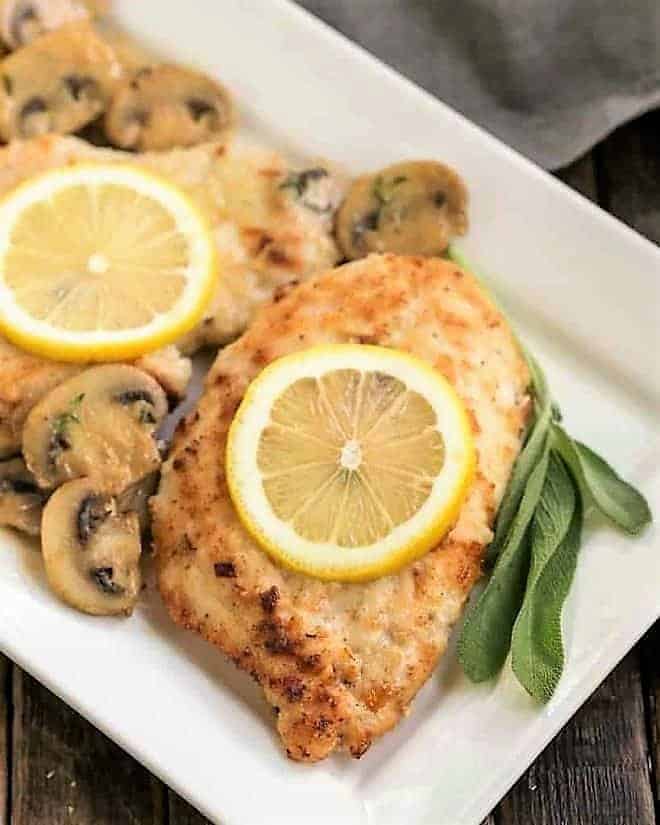 Creamy Chicken Marsala with Herbed Mushrooms topped with lemon slices on a white platter.