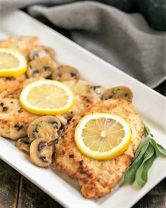 Creamy Chicken Marsala with Herbed Mushrooms on a white ceramic serving dish with lemons, mushrooms and sage