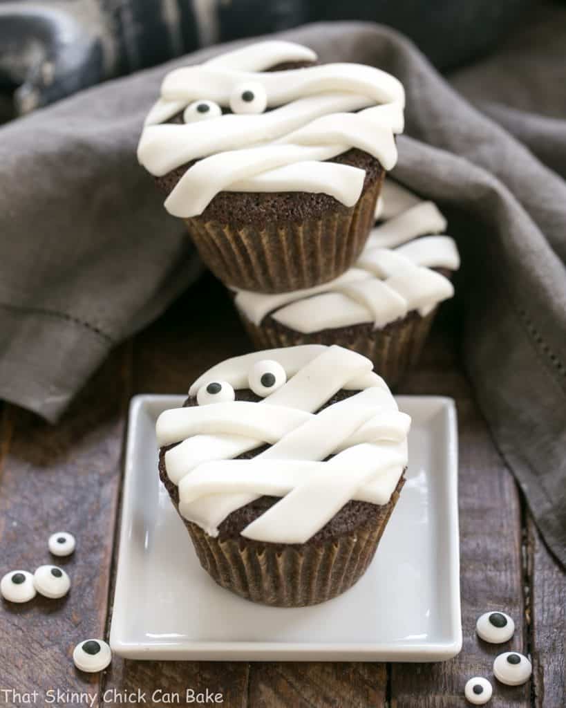 EASY Chocolate Mummy Cupcakes on a white plate and stacked with sugar eyes to garnish