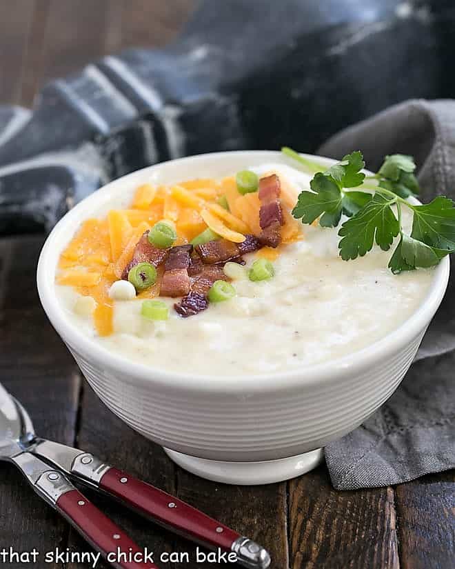 Side view of Loaded Baked Potato Soup in a white ceramic soup bowl with two red handled soup spoons.