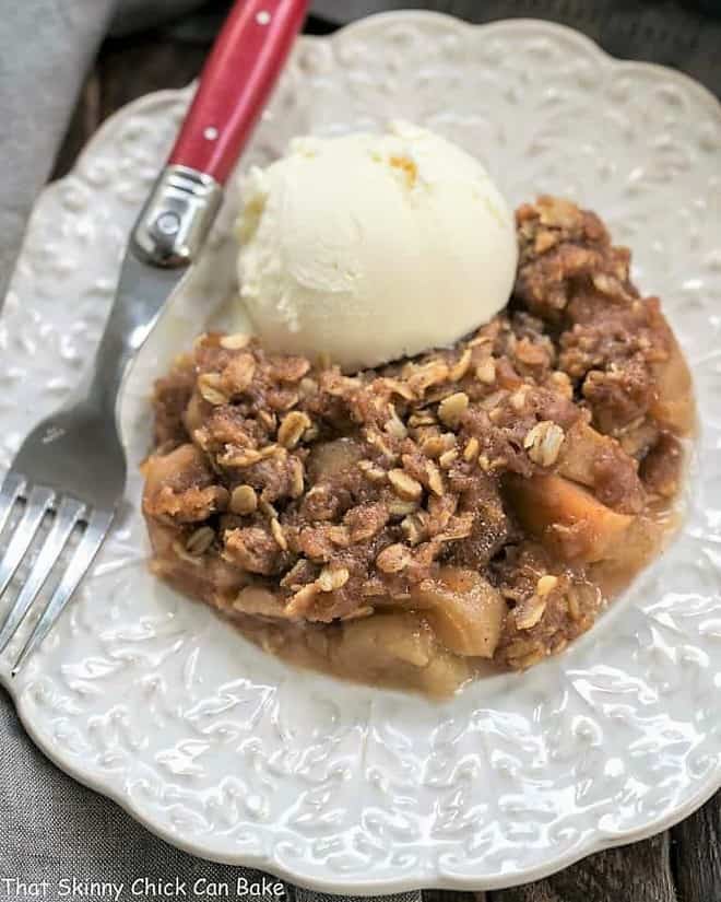 Easy Slow Cooker Apple Crisp with Oatmeal on a decorative white plate with vanilla ice cream and a red handled fork.