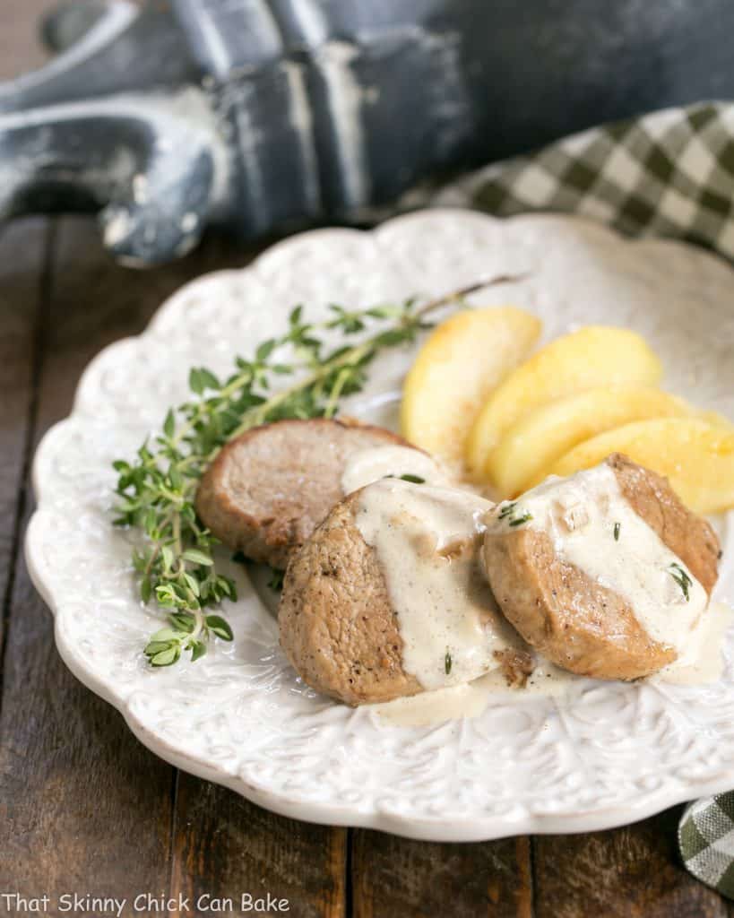Apple Topped Pork Medallions with Calvados Cream Sauce on a white plate garnished with thyme