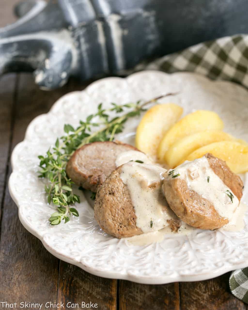 Apple Topped Pork Medallions with Calvados Cream Sauce on a white plate garnished with thyme.