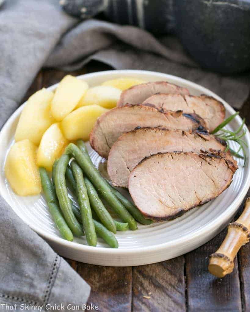 Pork tenderloin slices on a white dinner plate with beans and apples