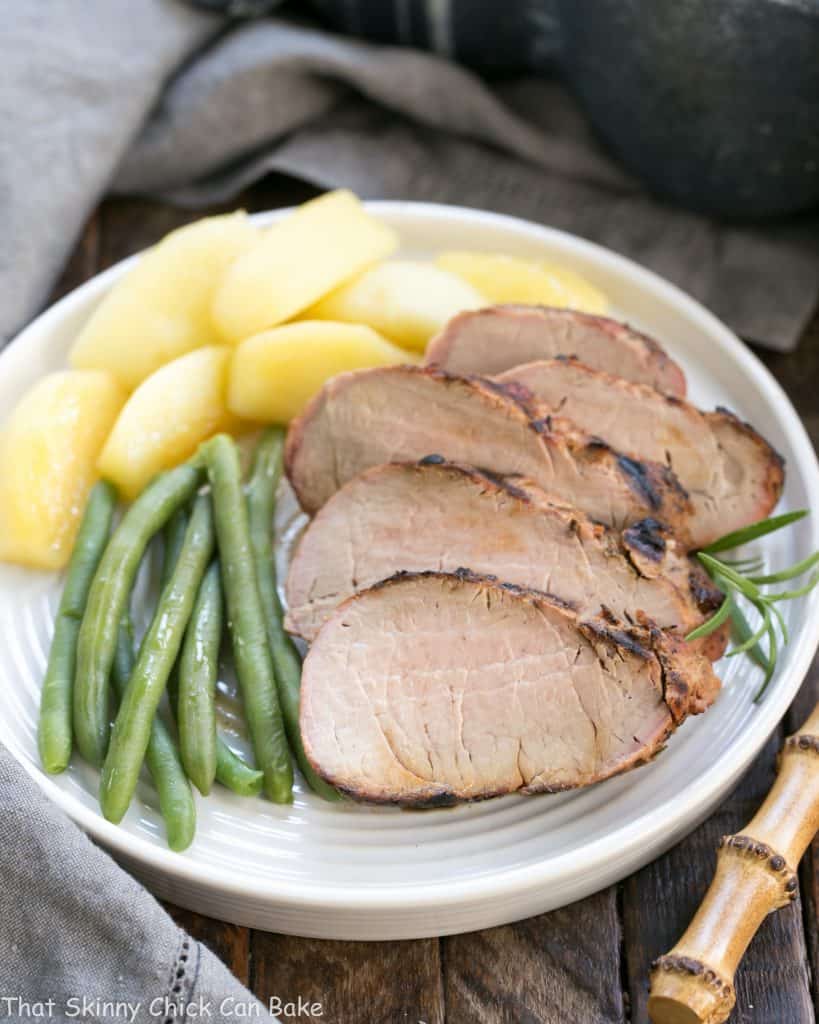 Sliced Maple Grilled Pork Tenderloin with apples and green beans on a white dinner plate