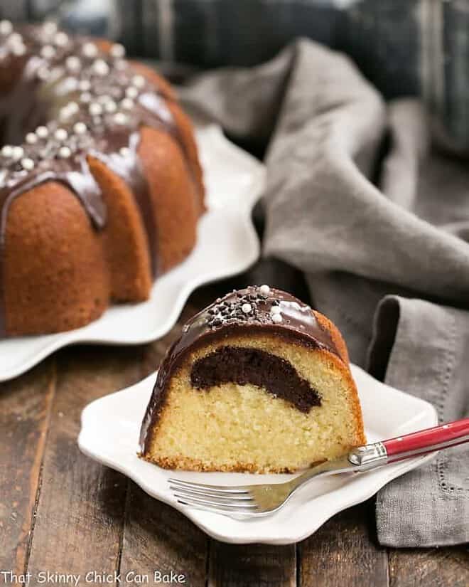 Tunnel of Fudge Cake - A rich butter cake with a fudgy ribbon in each slice. Rename as Tunnel of Doom cake for a fun Halloween dessert!! Slice of Tunnel of Fudge Cake on a square white plate with a red handled fork.