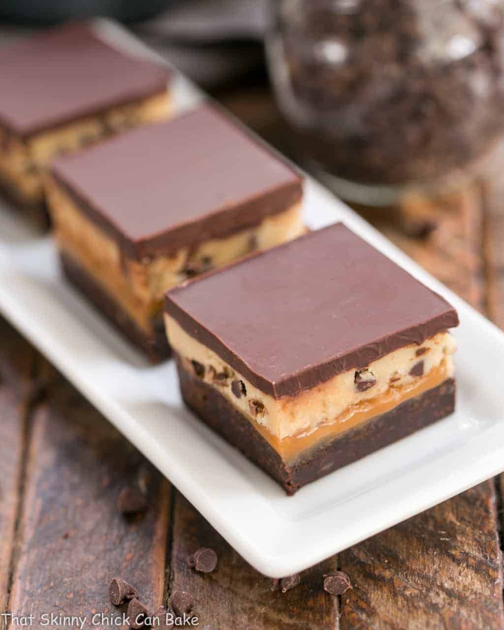 Cookie Dough Billionaire Bars lined up on a white, rectangular ceramic tray.