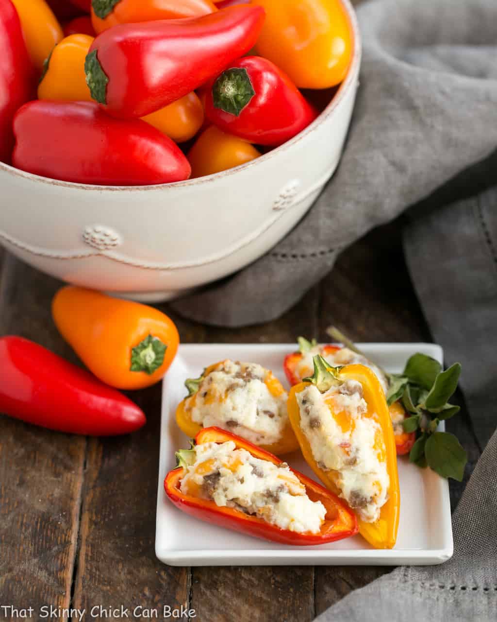 Cream Cheese Stuffed Mini Peppers with Sausage - An easy, flavorful appetizer for dinner with friends or game day entertaining! Cream Cheese Stuffed Mini Peppers with Sausage on a square plate with a bowl of mini peppers.