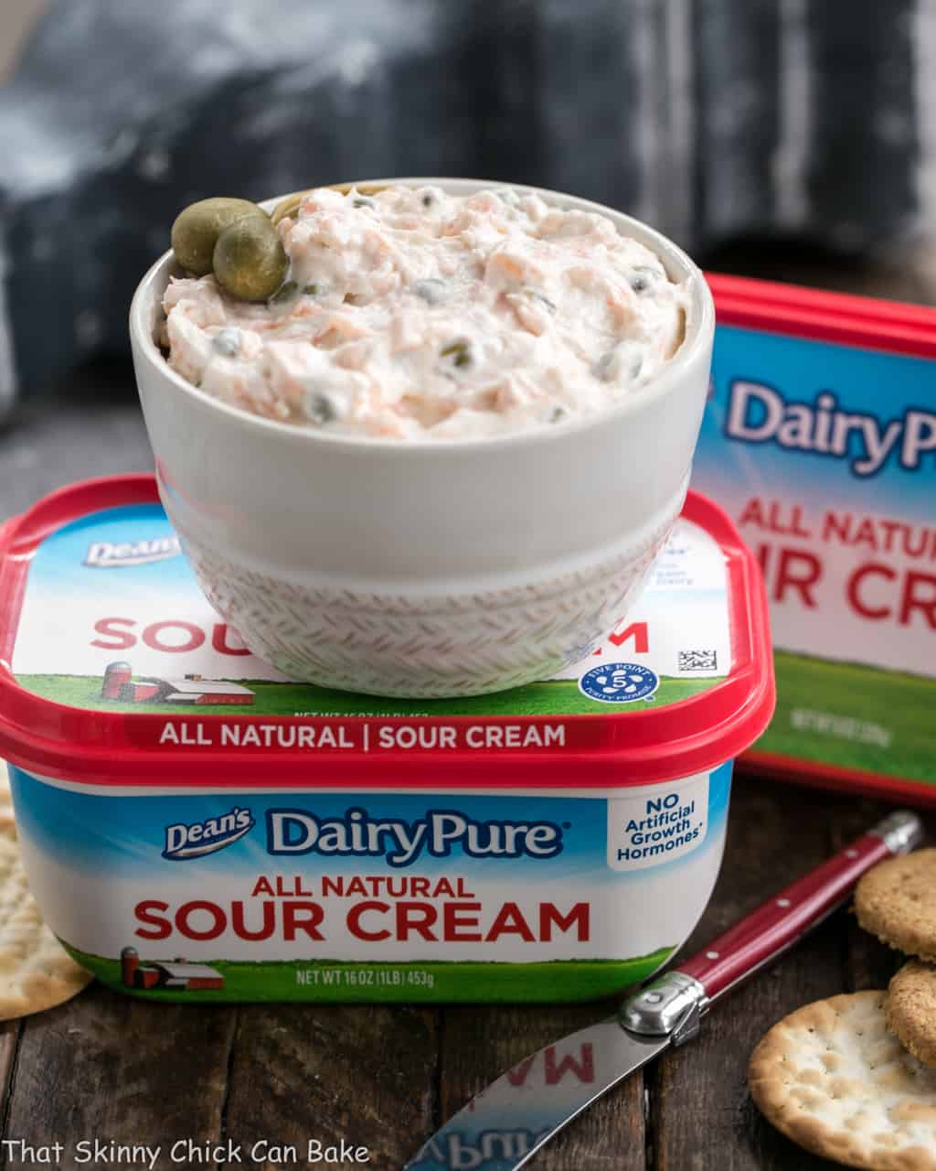 A bowl of Smoked Salmon Dip with Capers sitting on top of a container of DairyPure brand sour cream.