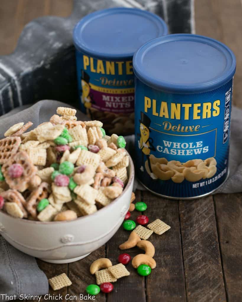 a bowl of party mix next to cans of Planter's roasted nuts