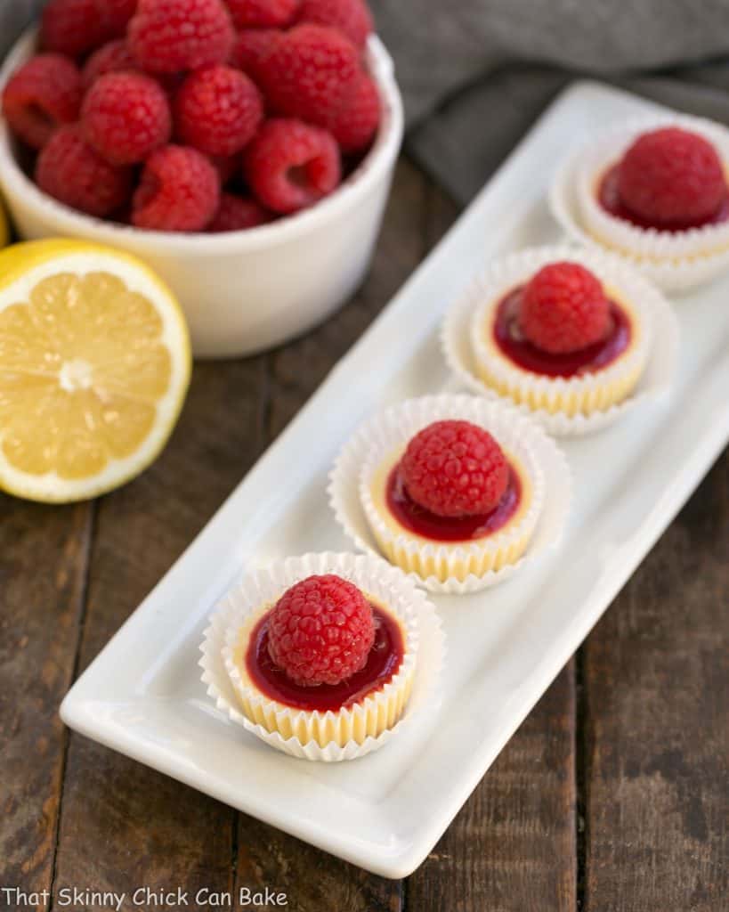 A white dessert platter holding raspberry topped mini cheesecakes