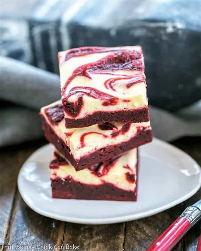 3 swirled red velvet cheesecake brownies stacked on a white tear drop shaped plate
