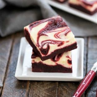 A stack of 2 red velvet cheesecake brownies on a square white plate