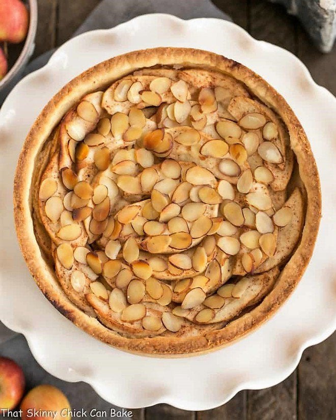 Cream Cheese Apple Torte - A buttery crust is topped with sweetened cream cheese, loads of cinnamon spiced apples, then sliced almonds Cream Cheese Apple Torte on a ruffled white cake stand viewed from above.