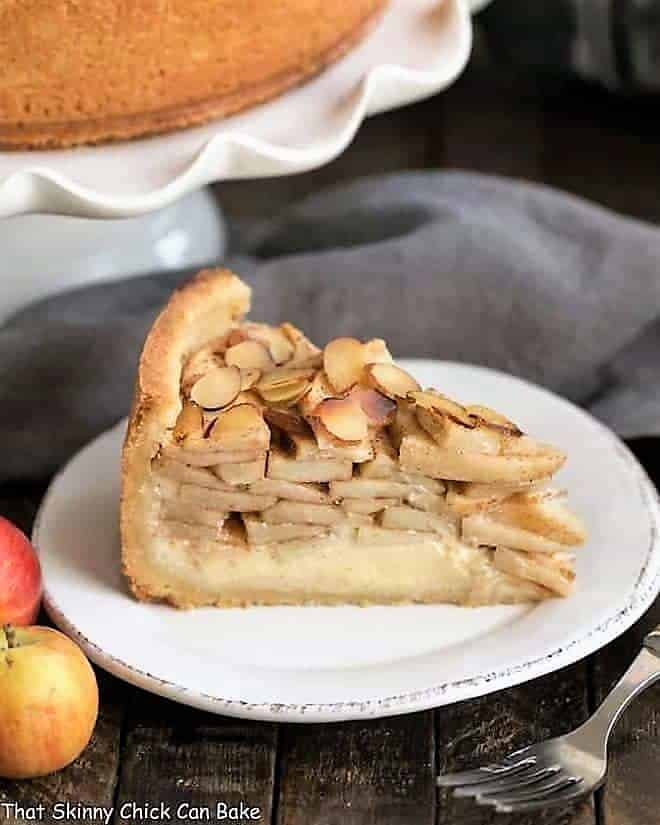 Cream Cheese Apple Torte on a white dessert plate with cake stand, apples and fork.