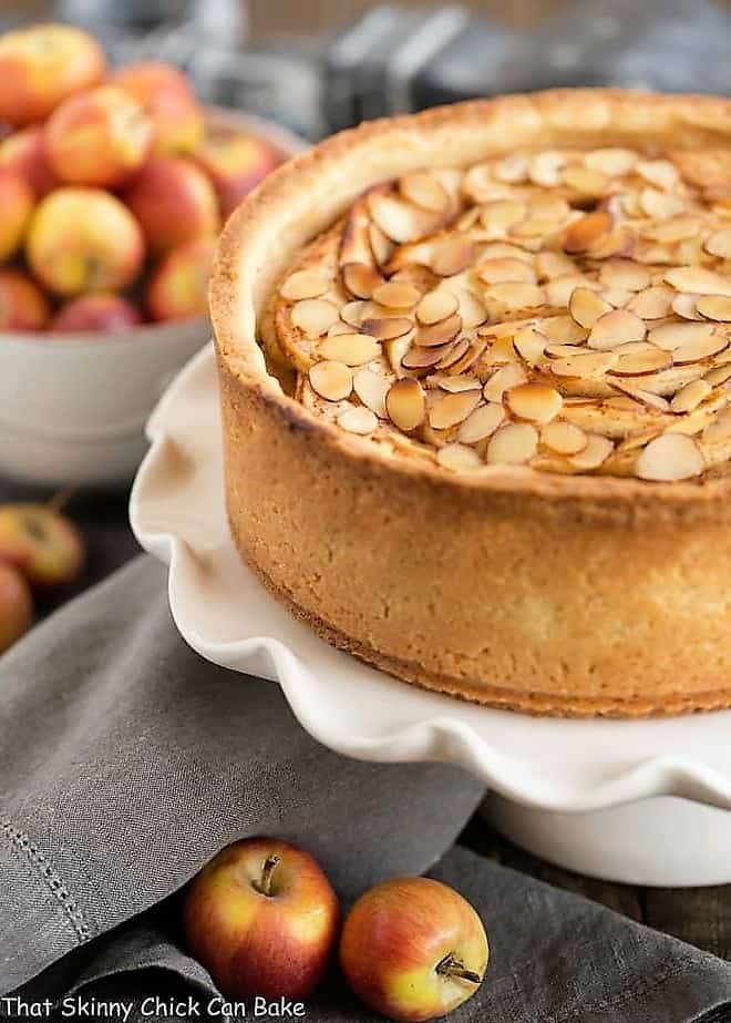 Cream Cheese Apple Torte on a ruffled white ceramic cake stand with lady apples to garnish.